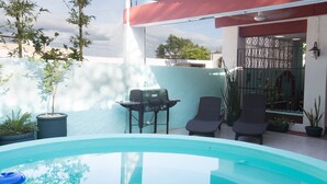 A swimming pool with a grill and chairs, surrounded by potted plants and a red awning. - Merida Serviced Apartments (Mérida)