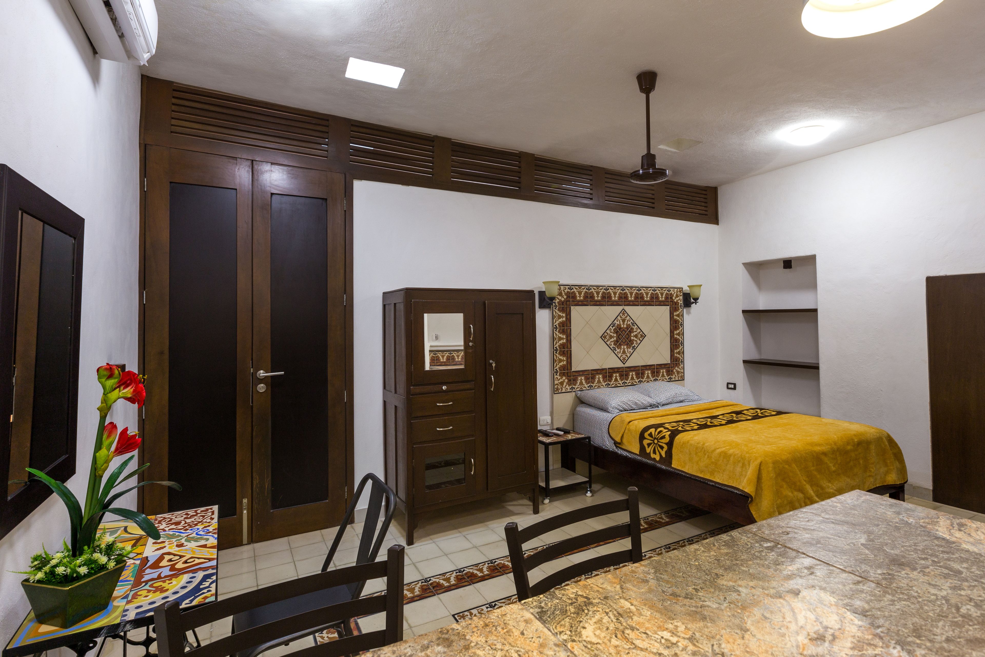 A bedroom with a bed, a desk, a chair, a wardrobe, and a potted plant.