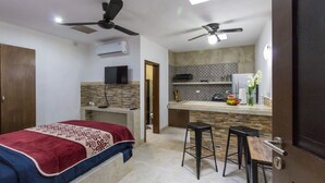 A compact room with a bed, a desk, two bar stools, a kitchenette, and two ceiling fans. - Merida Serviced Apartments (Mérida)