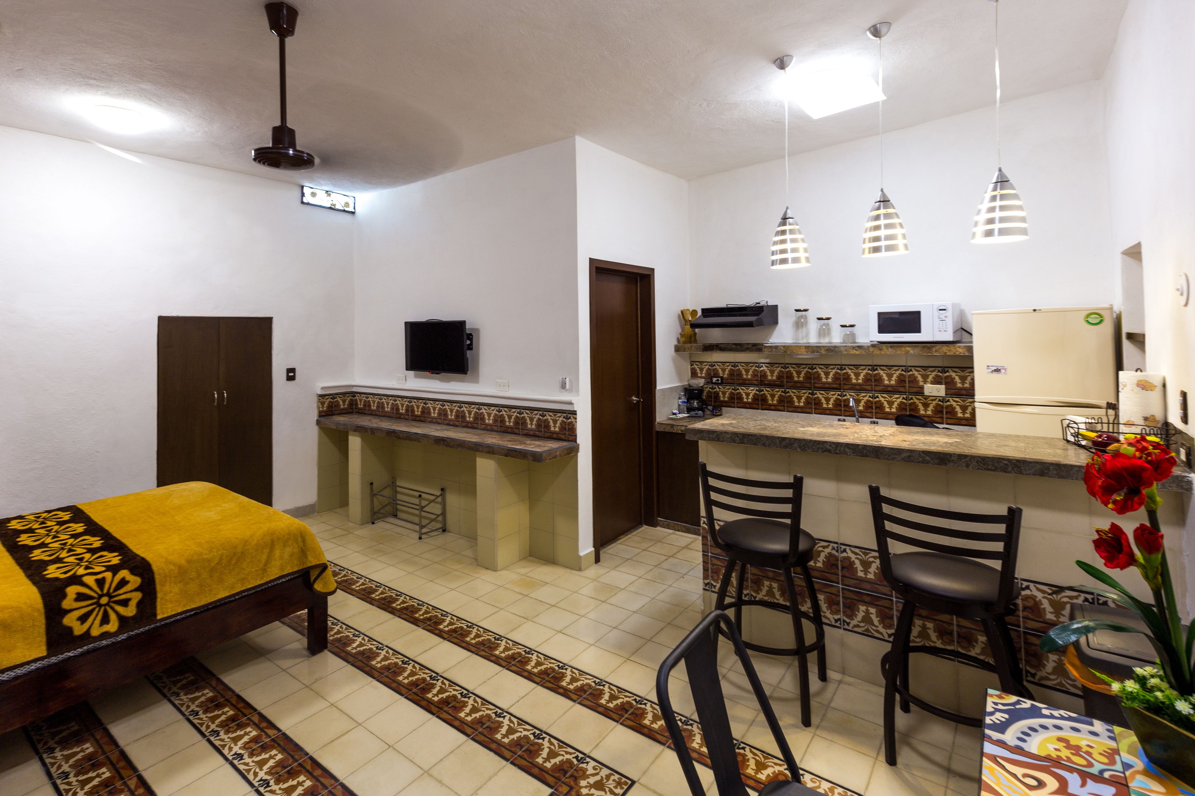 A compact hotel room with a bed, a small kitchenette, a TV, and a dining area with two chairs.