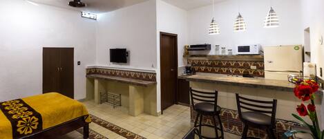 A compact hotel room with a bed, a small kitchenette, a TV, and a dining area with two chairs.