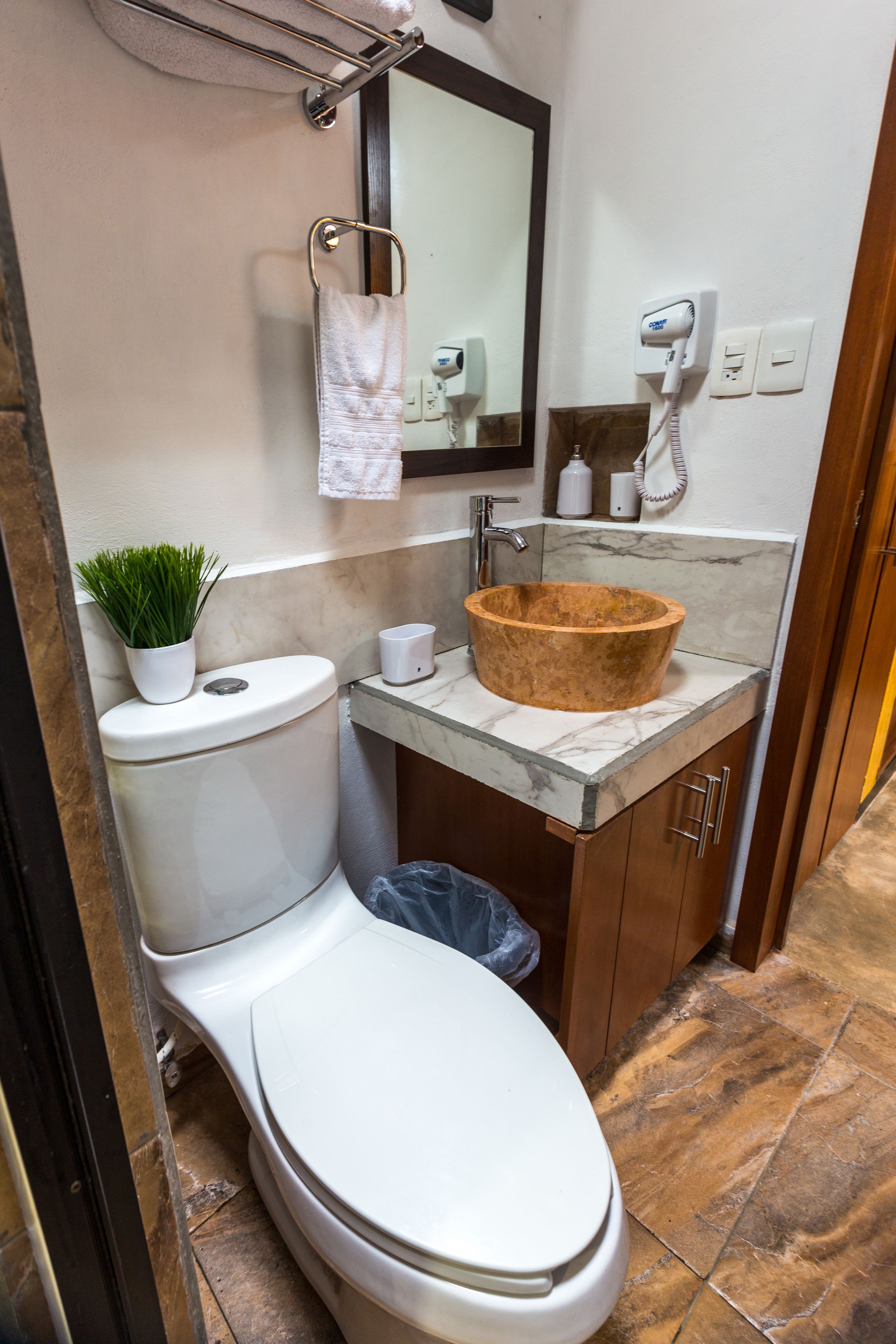 A bathroom with a toilet, a sink with a marble countertop, a towel rack, a hairdryer, and a trash bin.