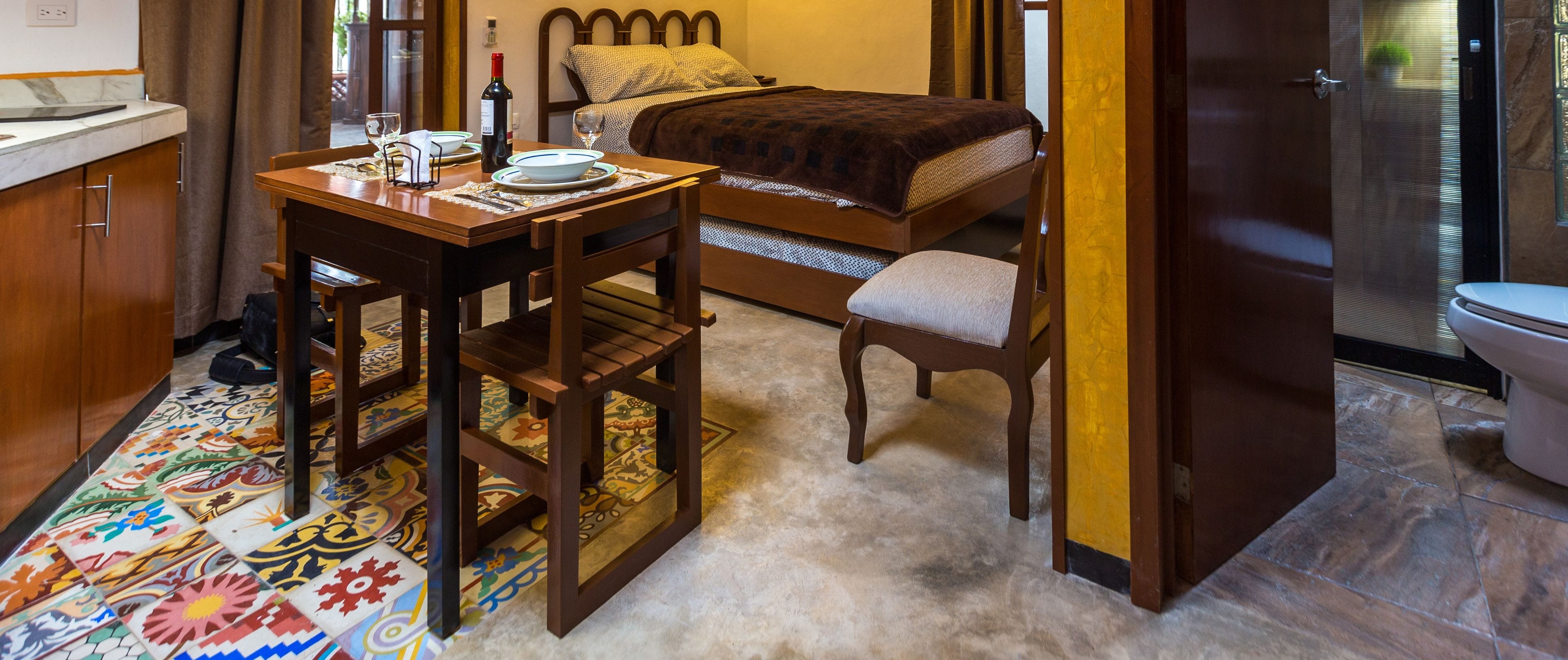 Una camera d'albergo con un letto, un piccolo tavolo con una bottiglia di vino, una sedia, un bagno con il water e una zona doccia.