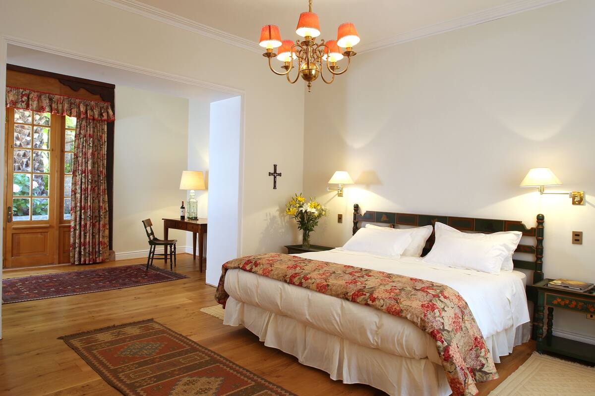 Ein Schlafzimmer mit einem großen Bett, einer Kristallleuchter, zwei Nachttischlampen, einem Kreuz an der Wand und einer Holztür mit Vorhängen.