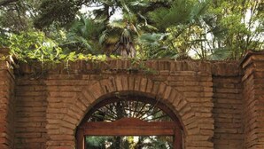 A brick archway leading to a pool area surrounded by lush greenery and stone walls. - Hotel Casa Real Viña Santa Rita (Buin)