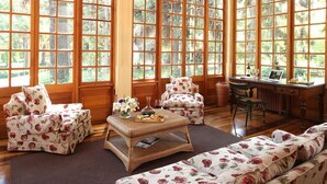 A spacious room with large windows, a wooden desk, a comfortable sofa, and a floral-patterned armchair. - Hotel Casa Real Viña Santa Rita (Buin)