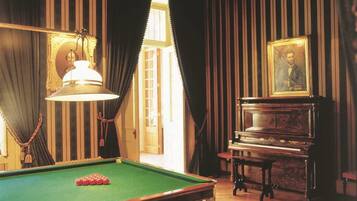 A room with a pool table, a piano, and a portrait on the wall.