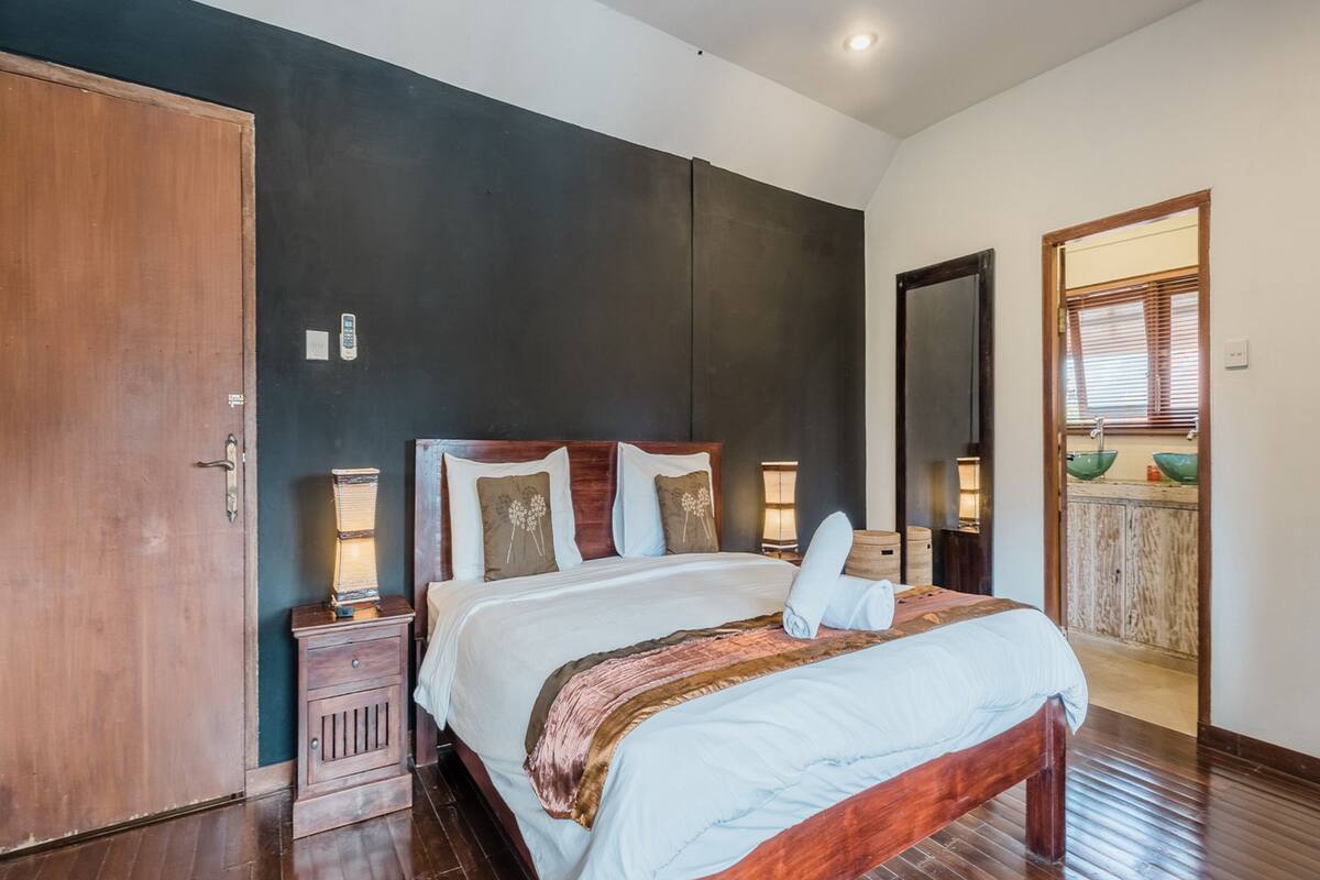 A bedroom with a wooden bed, a nightstand, a dresser, and a large mirror.