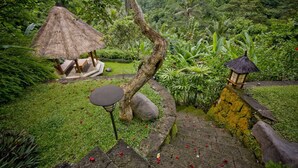 Un jardín exuberante con un pabellón de techo de paja, un banco de piedra y un farol.