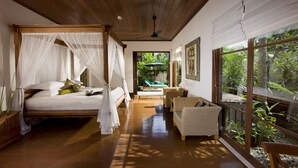 Un dormitorio con cama de dosel, una zona de estar con muebles de mimbre y amplias ventanas que ofrecen vistas al exterior.