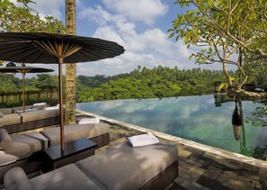 An infinity pool with lounge chairs and a table, surrounded by lush greenery and a clear sky. - Bukit Naga Villa-Private Pool (Bangli)