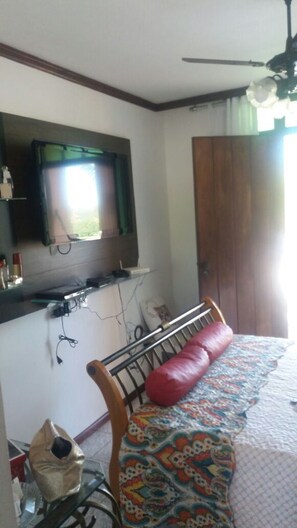 A bedroom with a bed, a television mounted on the wall, a wooden door, and a window with curtains. - Premium Cabo Frio (Cabo Frio)