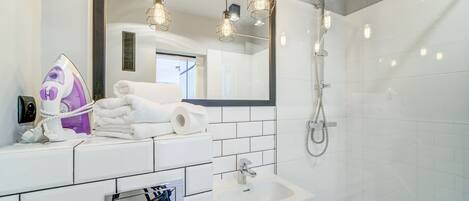 A modern bathroom with a white tiled wall, a sink, a mirror, and a shower.