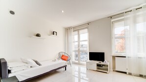 Una habitación moderna y bien iluminada con una cama, un televisor y una ventana que ofrece vistas a edificios.