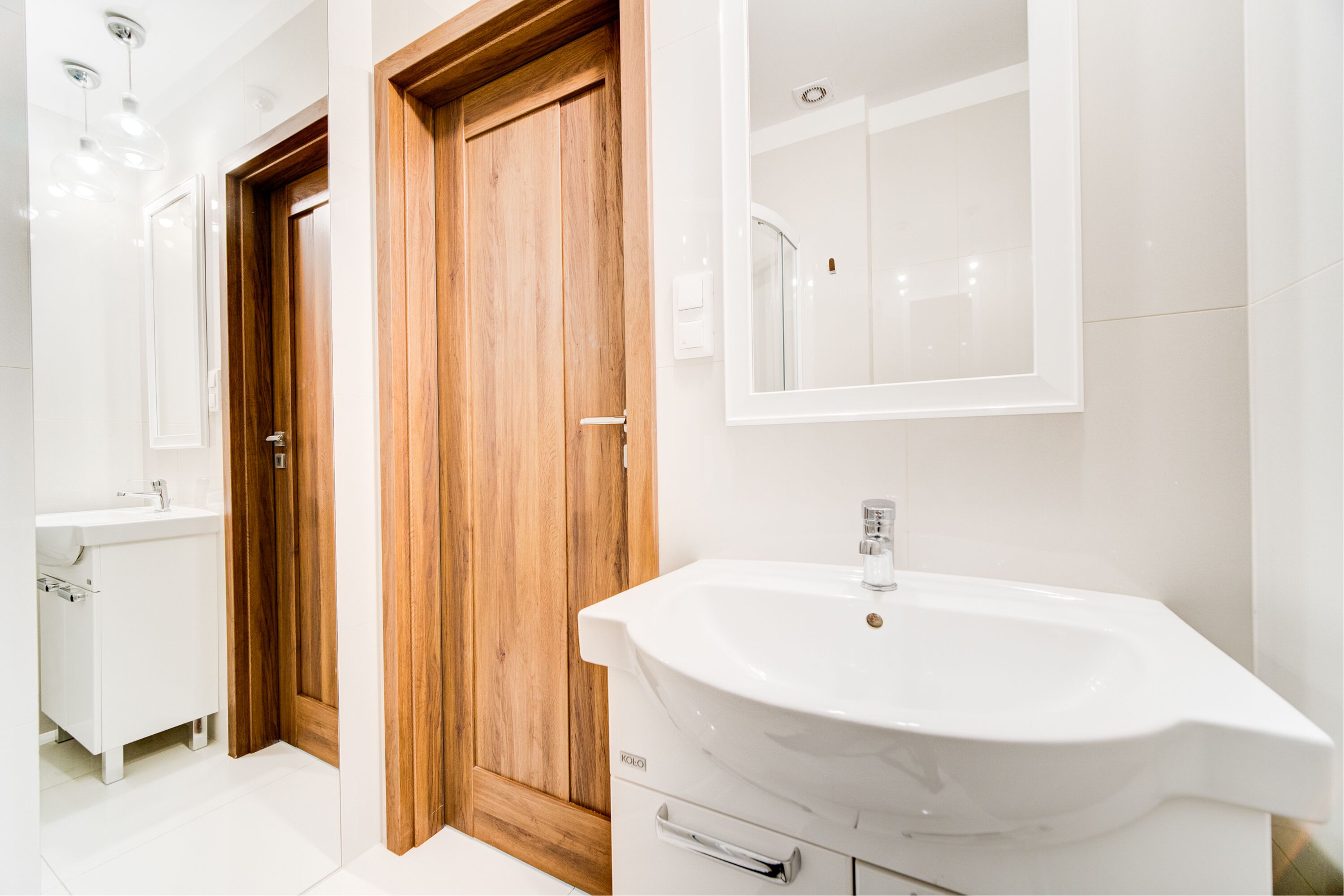 Un baño moderno con puerta de madera, un lavabo blanco y un espejo encima.