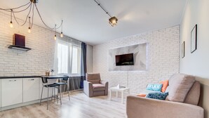 Una sala de estar moderna con una zona de cocina, un sofá, un sillón y un televisor montado en la pared.
