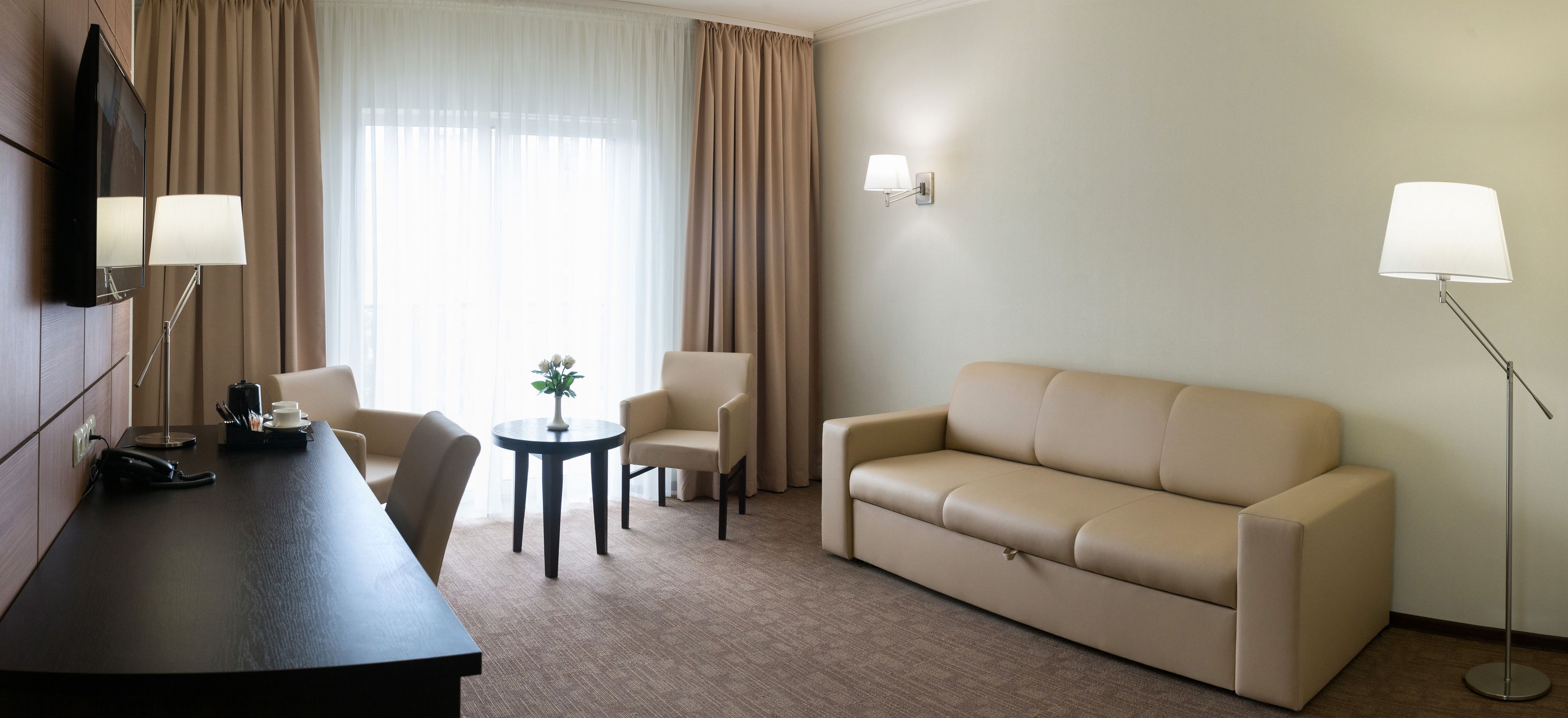 A hotel room with a sofa, two armchairs, a small round table, a desk with a telephone, and a lamp.