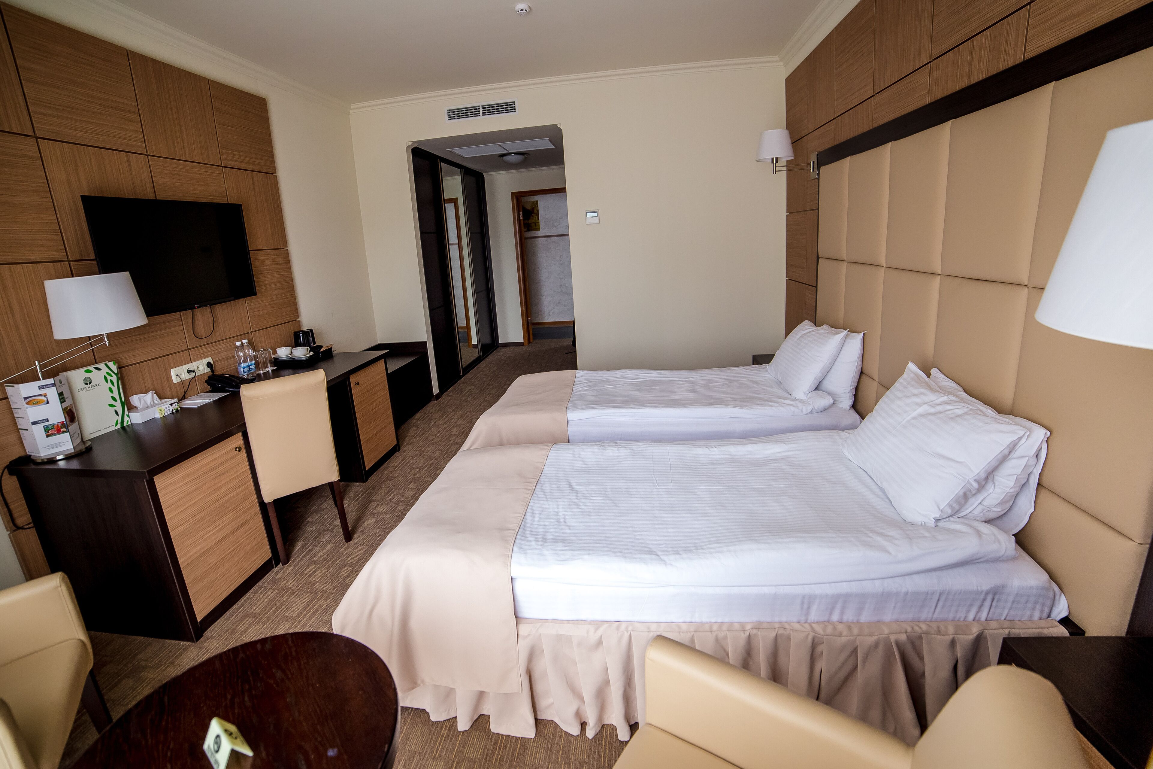 A hotel room with two beds, a desk, a TV, and a chair.