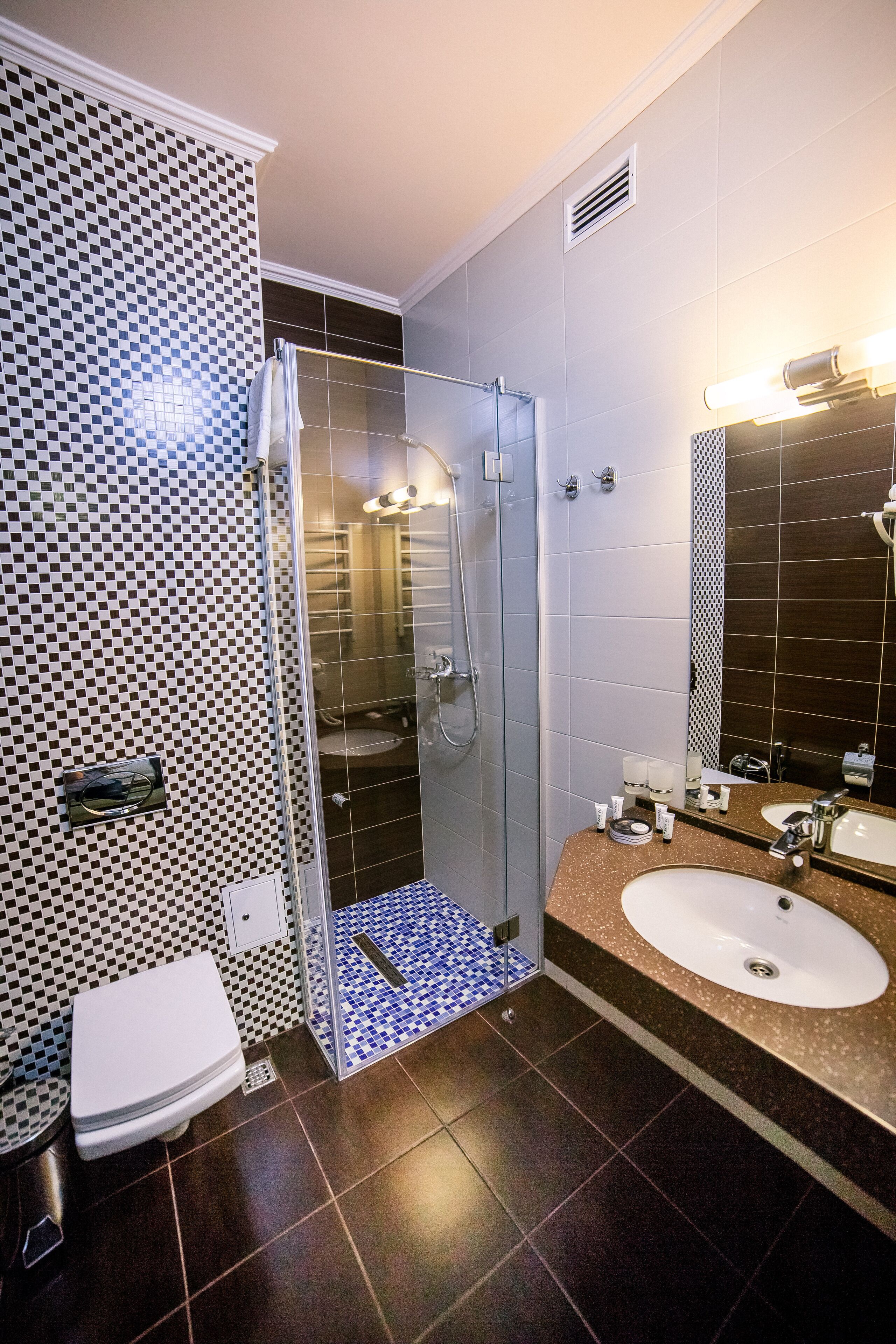 Un bagno moderno con doccia vetrata, un water bianco e due lavandini con piano in granito.