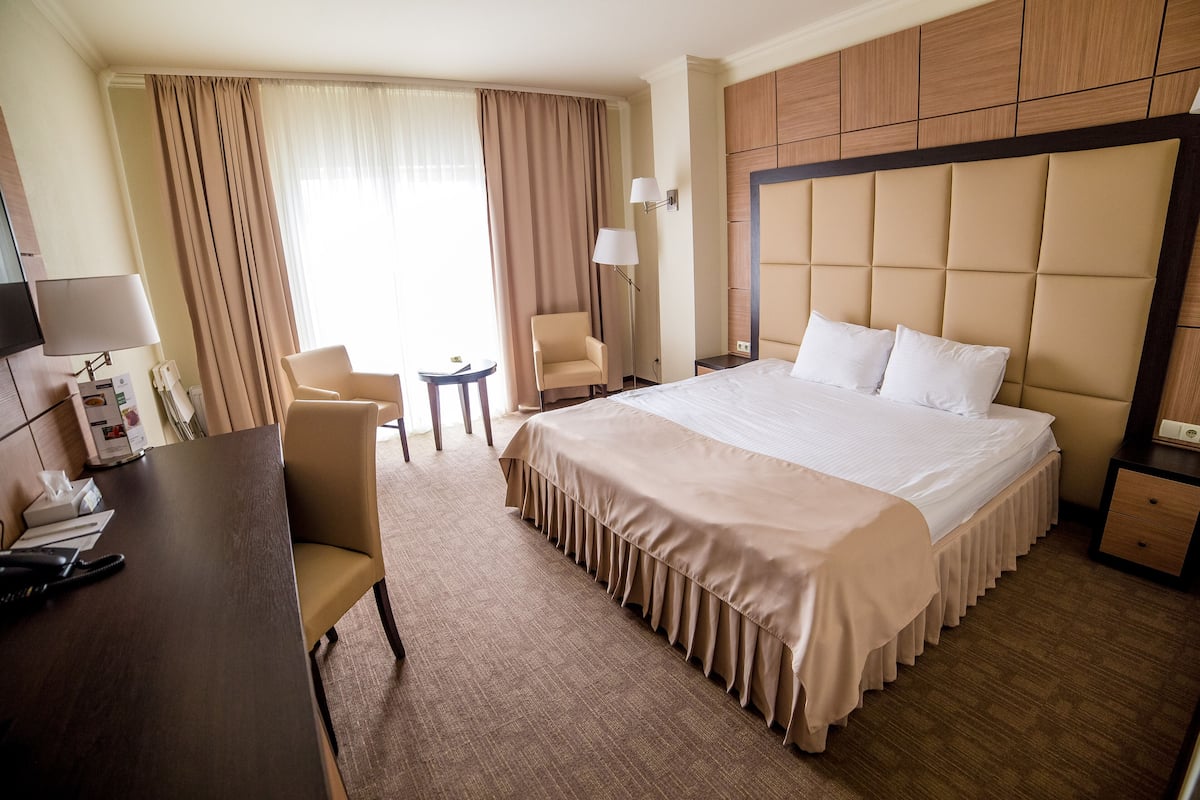 Habitación de hotel con una cama grande, un escritorio, una silla, una mesita de noche y una lámpara.