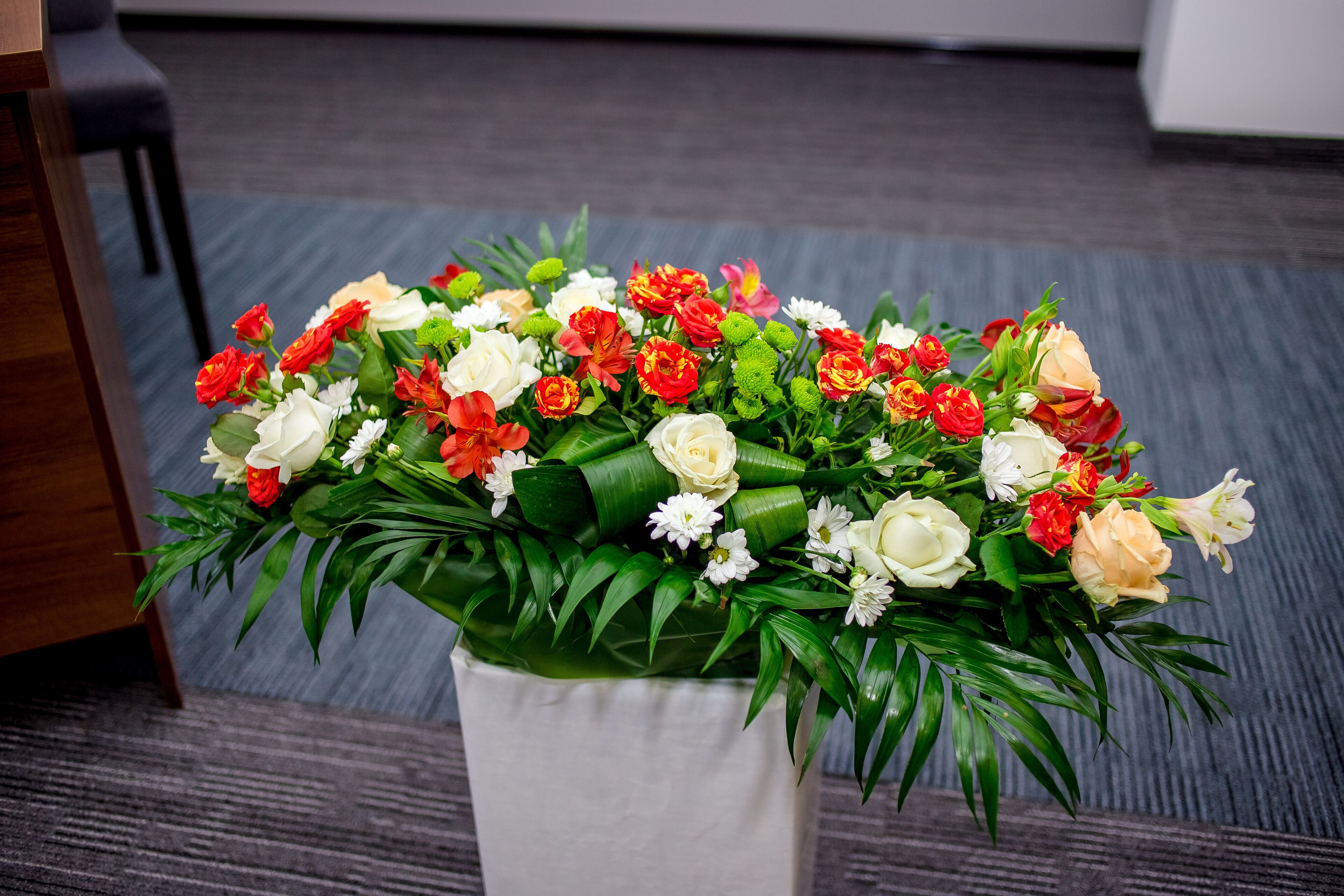 Un bouquet de fleurs dans un vase blanc, posé sur un sol recouvert d’une moquette.