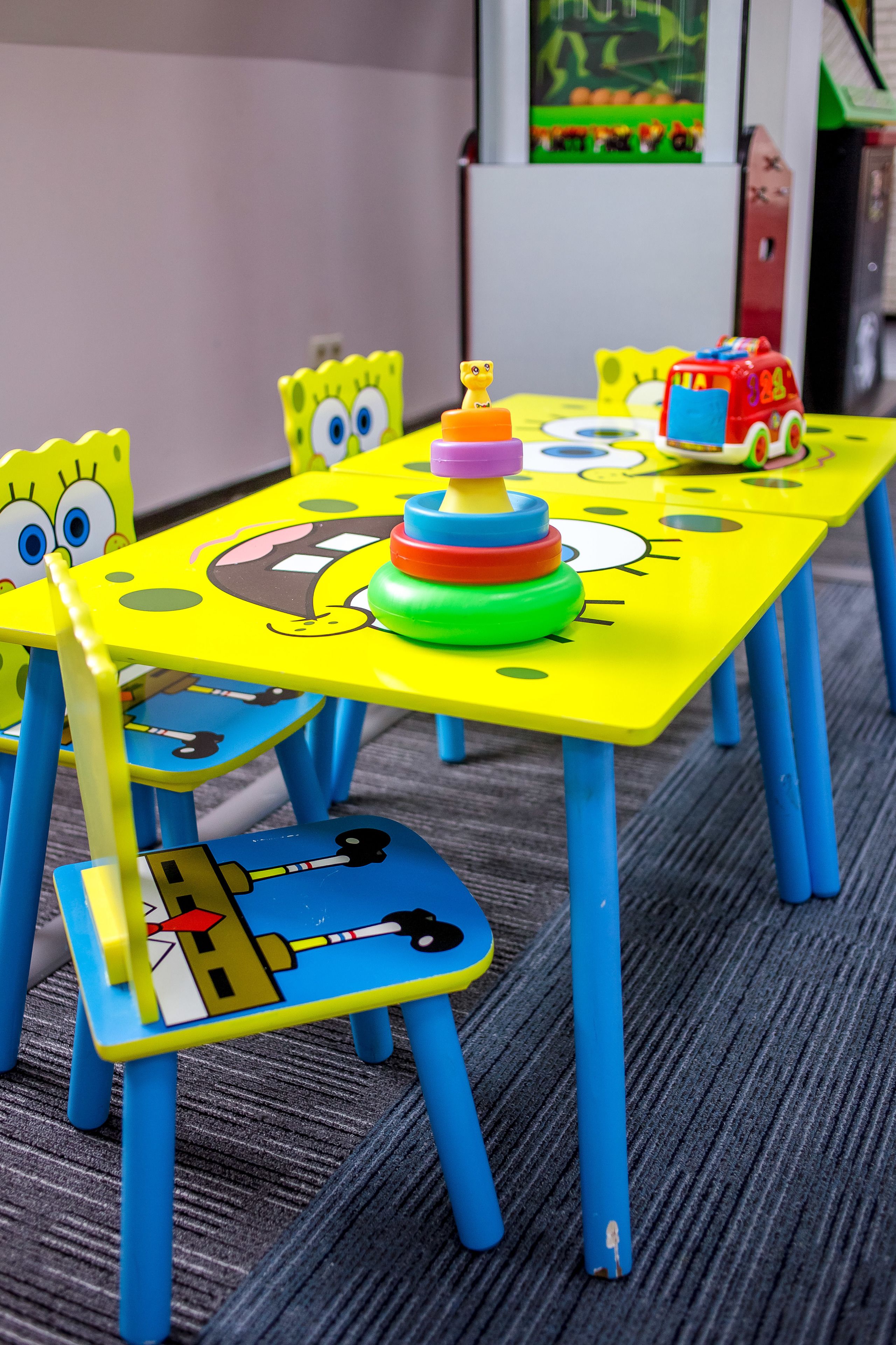 Una mesa infantil con diseño de Bob Esponja, que incluye un juguete para apilar aros, un camión de bomberos de juguete y un martillo de juguete.