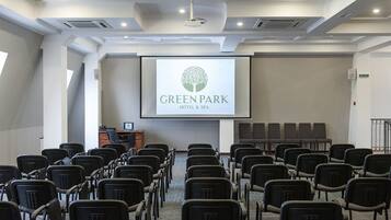 A conference room with rows of chairs, a projector screen displaying the GreenPark Hotel & Spa logo, and a podium at the front.