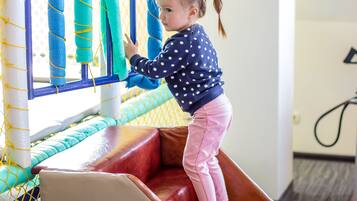 A child climbing a red staircase in a play area with netted walls and padded steps.
