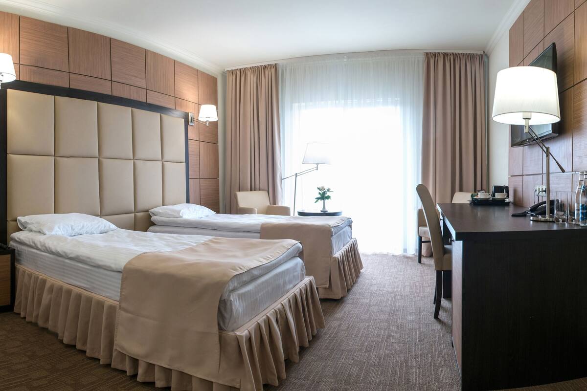 Habitación de hotel con dos camas, un escritorio, una silla, un televisor y una lámpara.