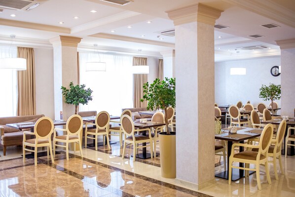 A hotel dining area with multiple tables and chairs, large windows with curtains, and potted plants. - Green Park Hotel (Truskavets)