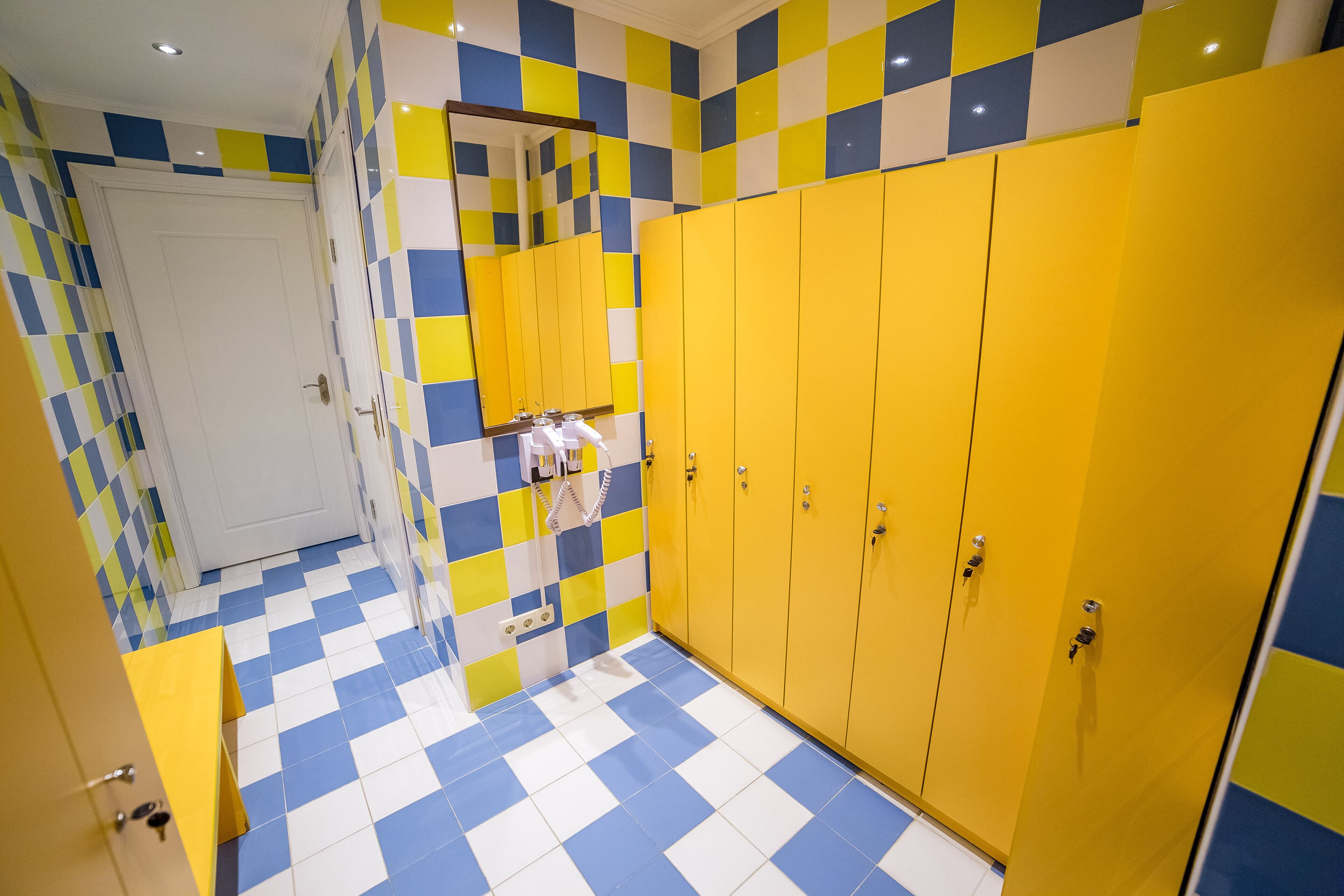 A bathroom with yellow lockers, a white door, and a blue and yellow checkered floor.