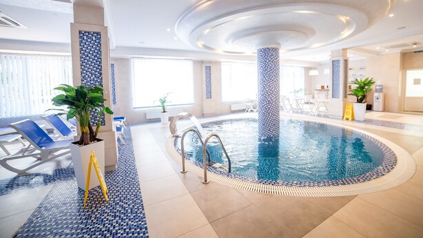 An indoor swimming pool with a tiled floor, lounge chairs, and a plant. - Green Park Hotel (Truskavets)