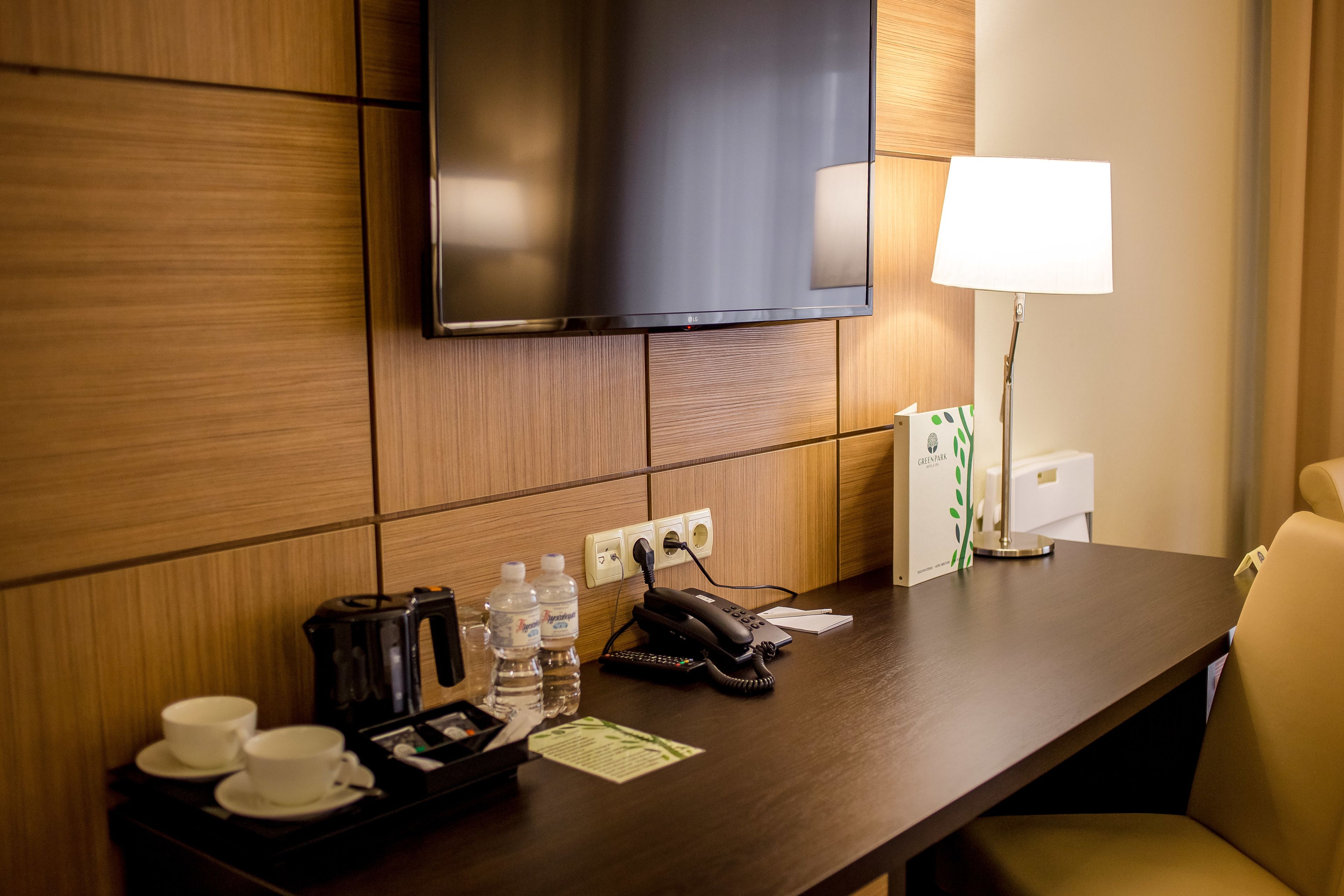Ein Hotelzimmer mit einer Wandpaneele aus Holz, einem Flachbildfernseher über einem Holztisch, einer Lampe und einem Stuhl.