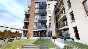 A multi-story residential building with balconies, a small garden area with a bench, and a clear sky. - Rint - Centrum Nowy Świat (Bialystok)