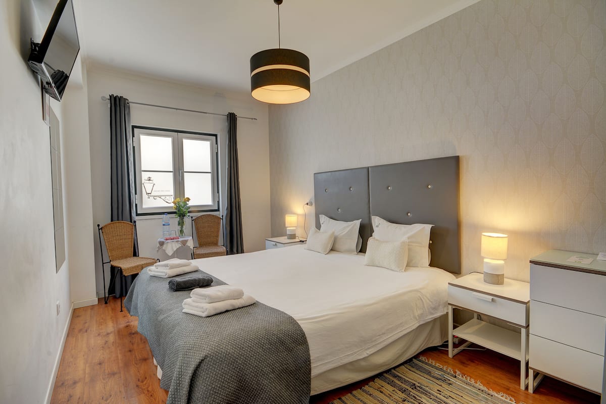 Een moderne hotelkamer met een groot bed, een flatscreen televisie aan de muur, een nachtkastje met een lamp en een raam met gordijnen.