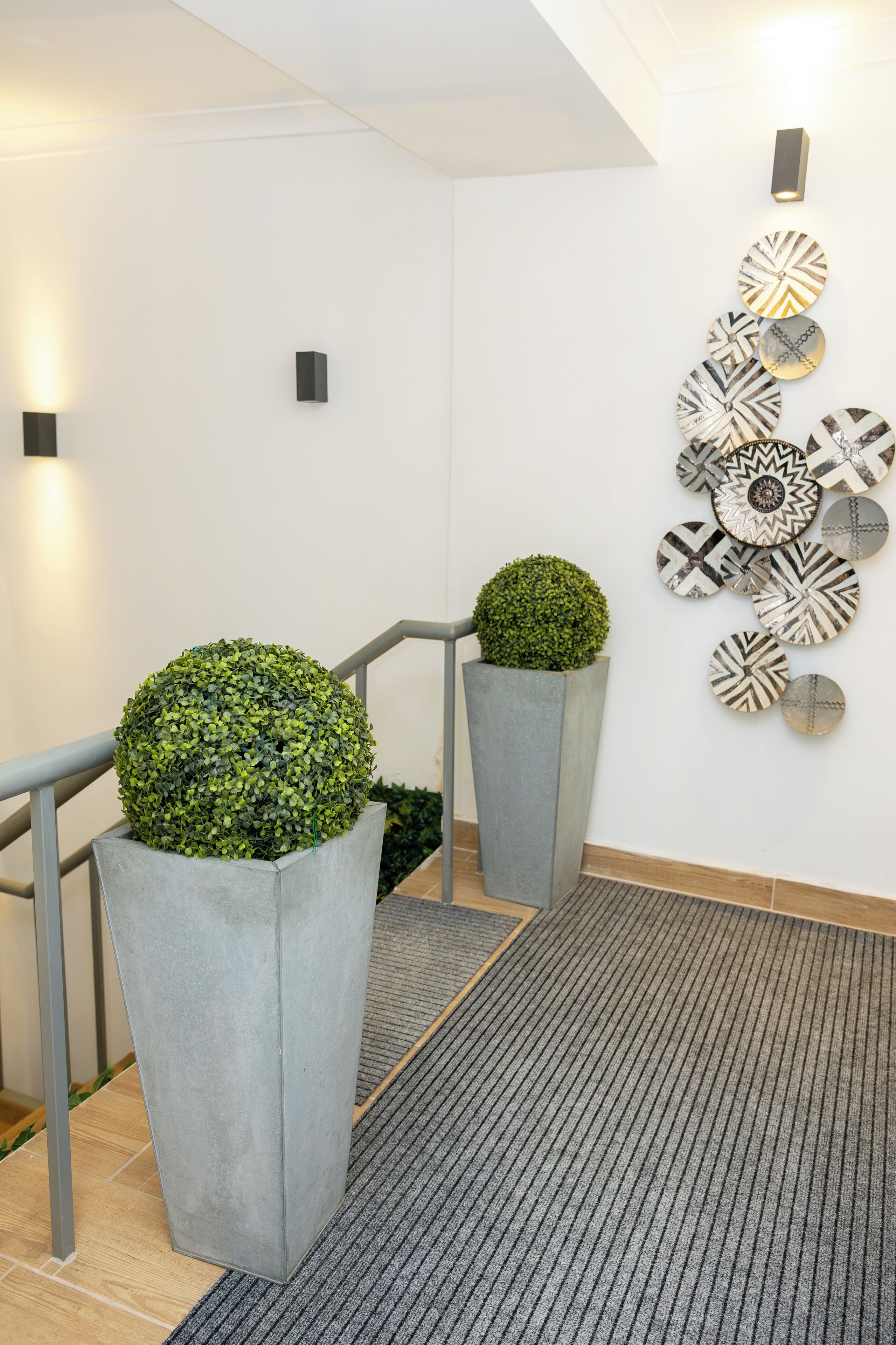 A modern interior with a staircase, grey concrete planters with spherical greenery, and a wall decorated with patterned circular art.