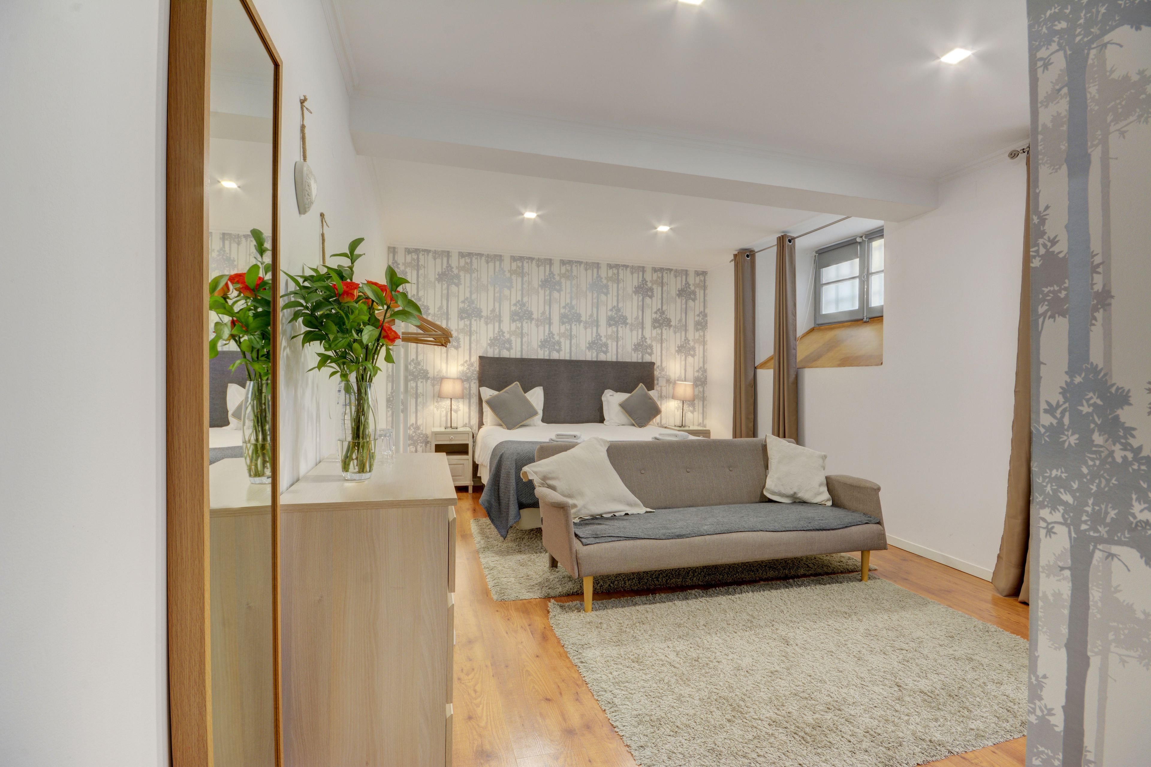 A modern bedroom with a bed, bedside tables, a sofa, and a mirror.