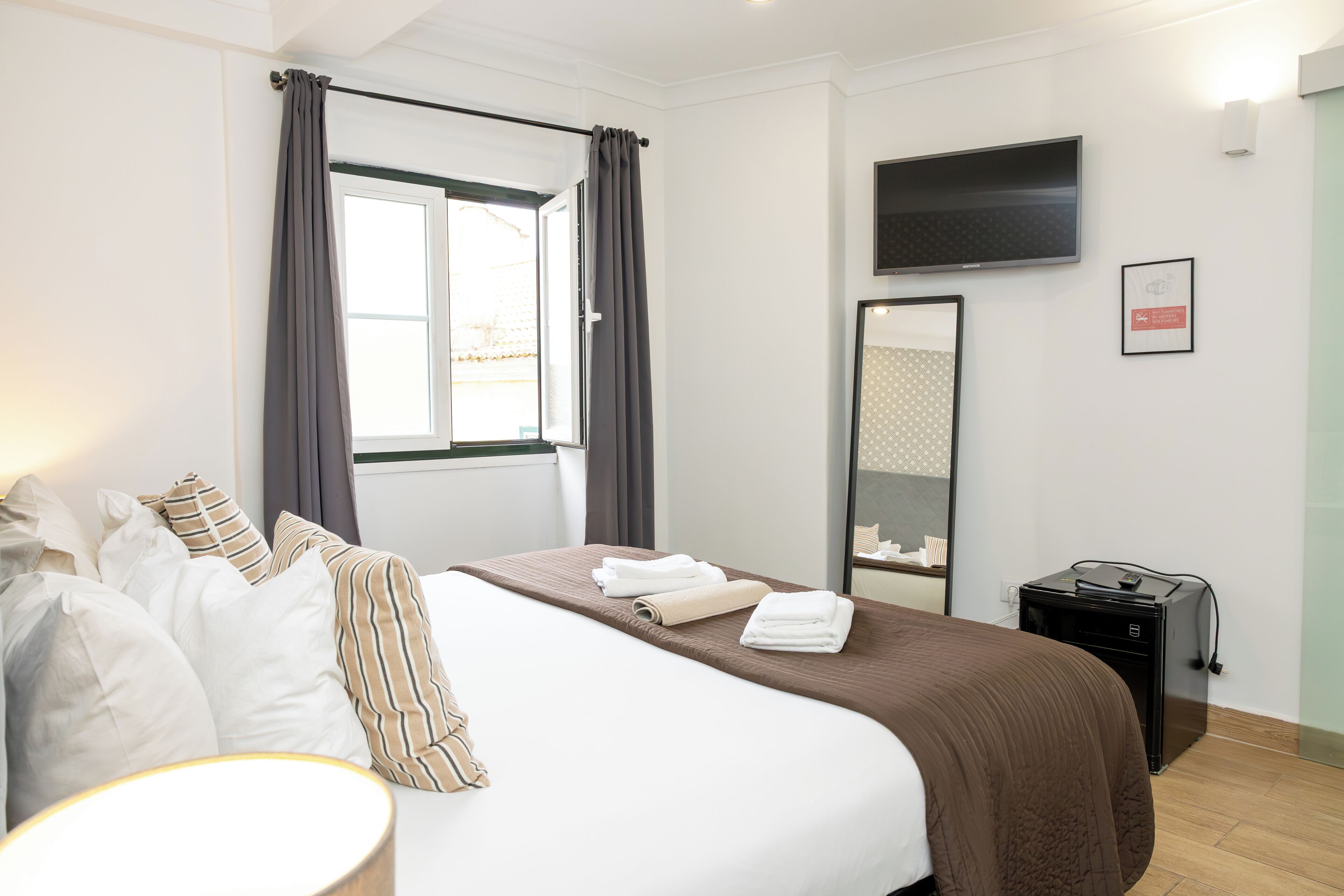 Ein Hotelzimmer mit Bett, Flachbildfernseher, Spiegel und Schreibtisch mit Lampe.