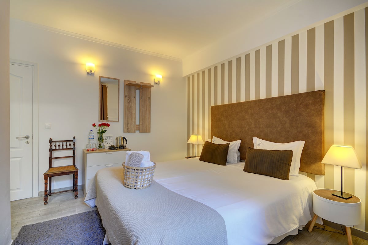 Een hotelkamer met een groot bed, twee bedlampen, een houten stoel, een kleine tafel met een lamp en een spiegel aan de muur.