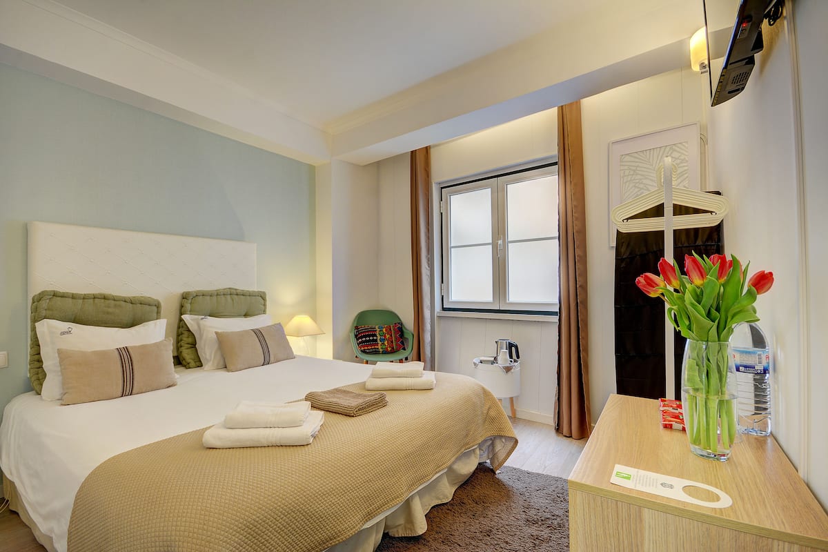Een hotelkamer met een bed, een nachtkastje met een bloemenvaas, een stoel en een raam met gordijnen.
