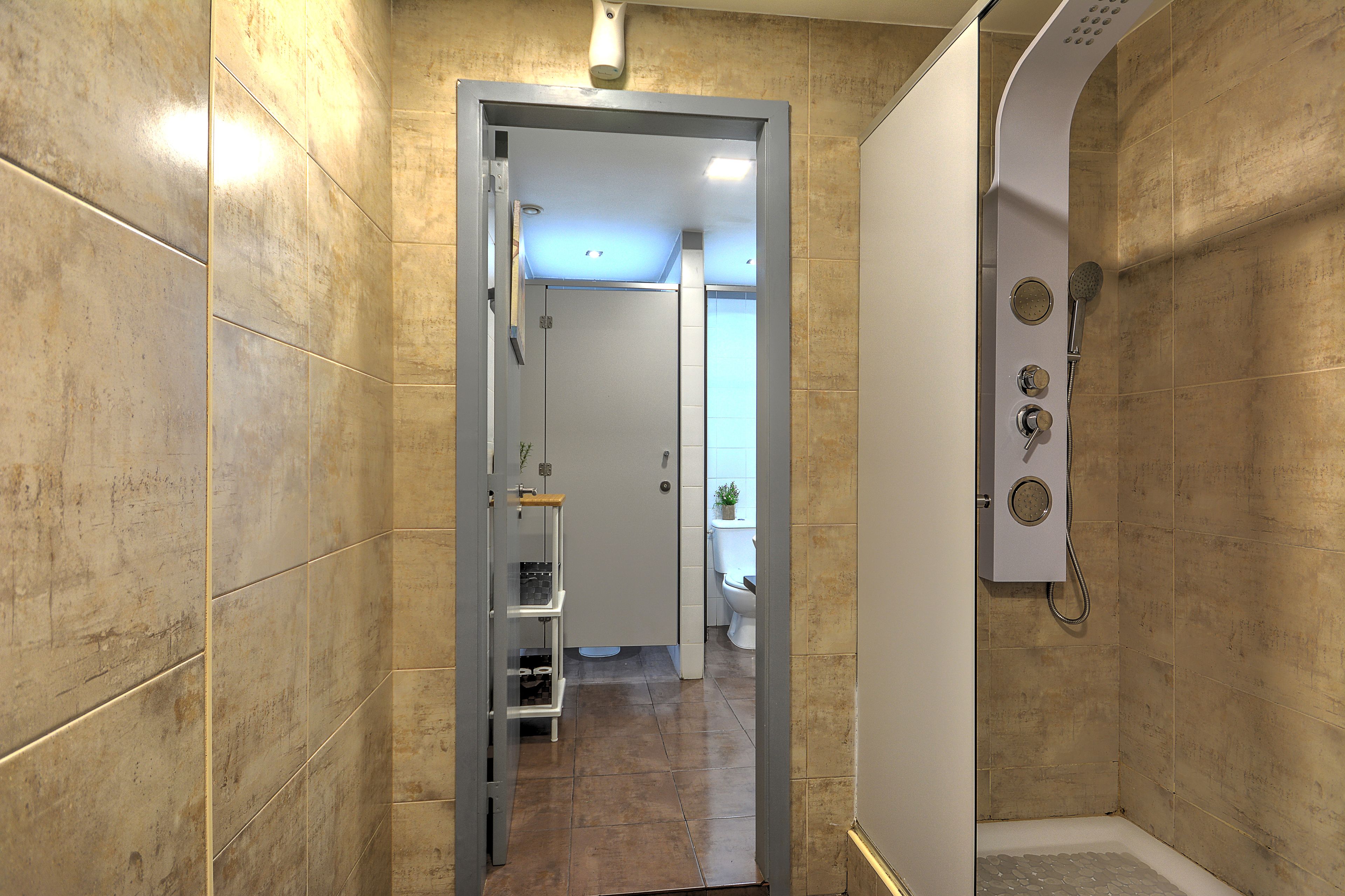 A bathroom with beige tiles, a shower enclosure, and a toilet visible in the background.