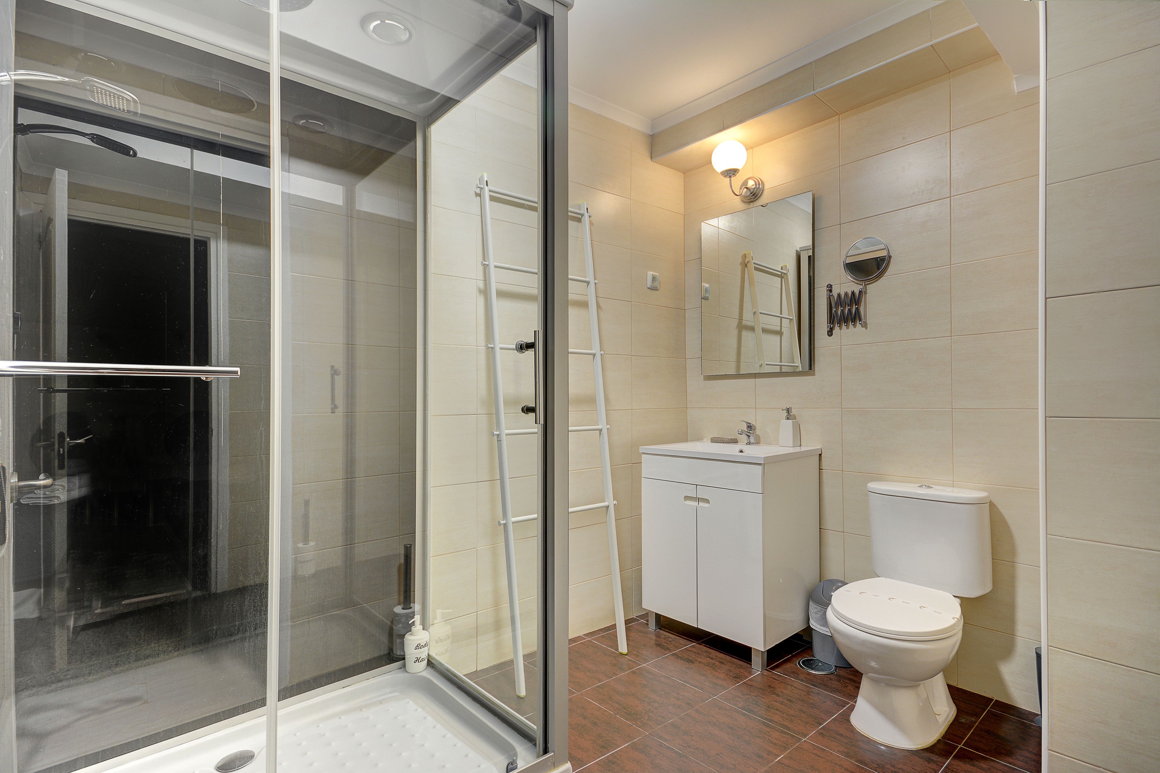Une salle de bain avec une douche à parois de verre, un lavabo blanc, des toilettes et un miroir au-dessus du lavabo.
