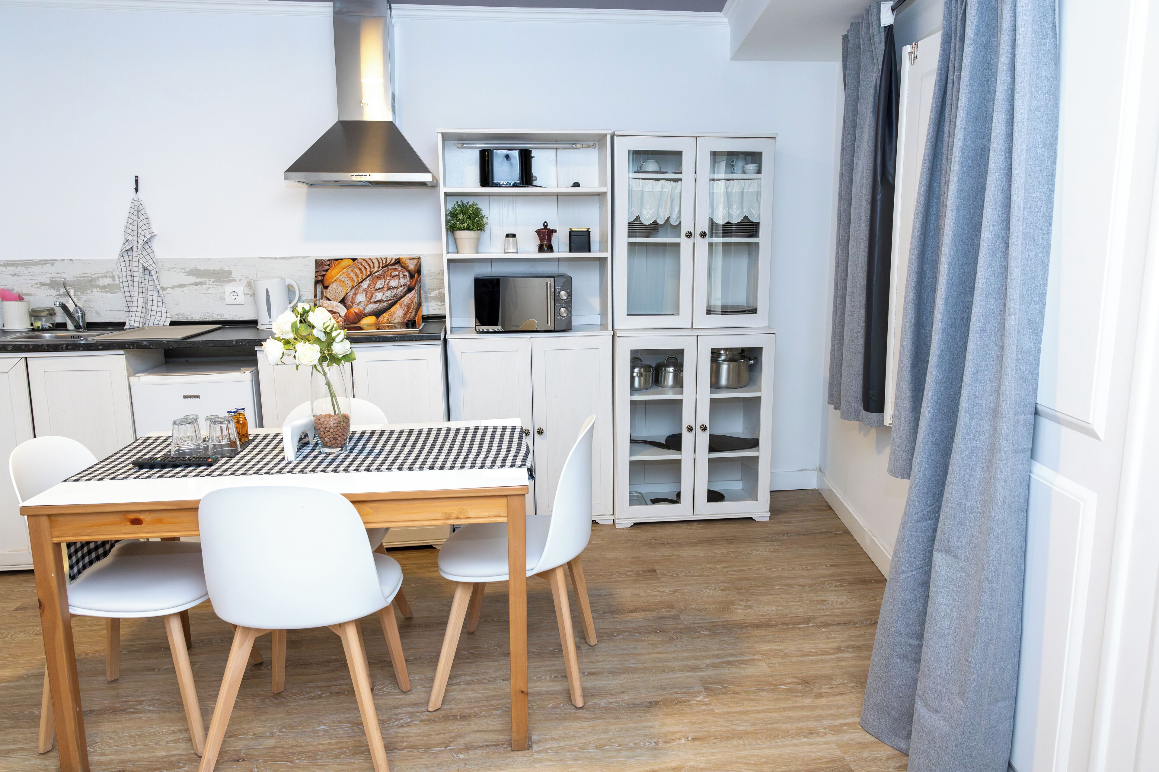 Eine moderne Küche mit weißen Schränken, einer Mikrowelle und einem Essbereich mit einem Holztisch und weißen Stühlen.