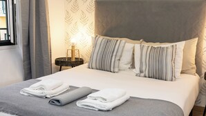 A neatly made bed with a grey and white striped pillow, a grey blanket, and two folded white towels.