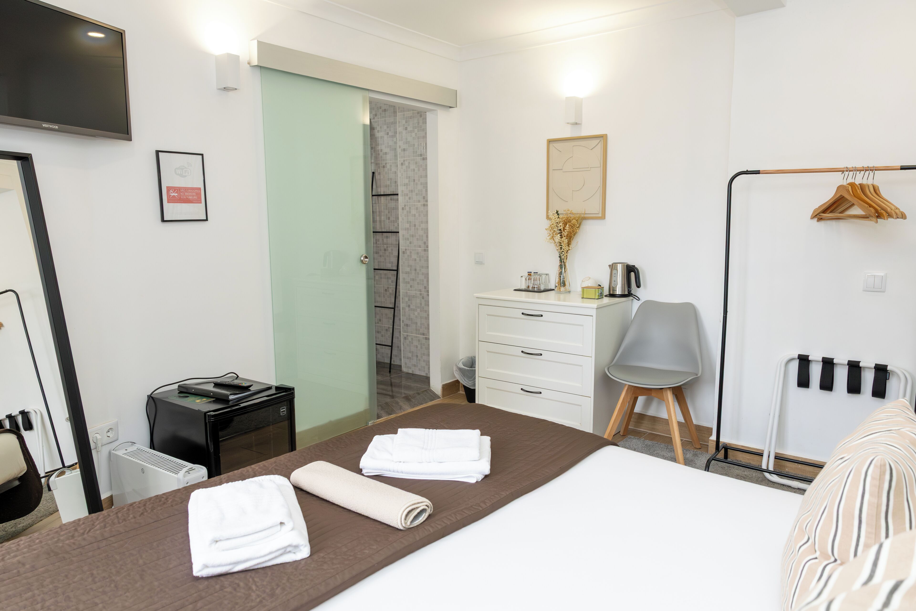 Une chambre d’hôtel avec un lit, un bureau, une chaise, un radiateur, une télévision et une salle de bain visible à travers une porte ouverte.