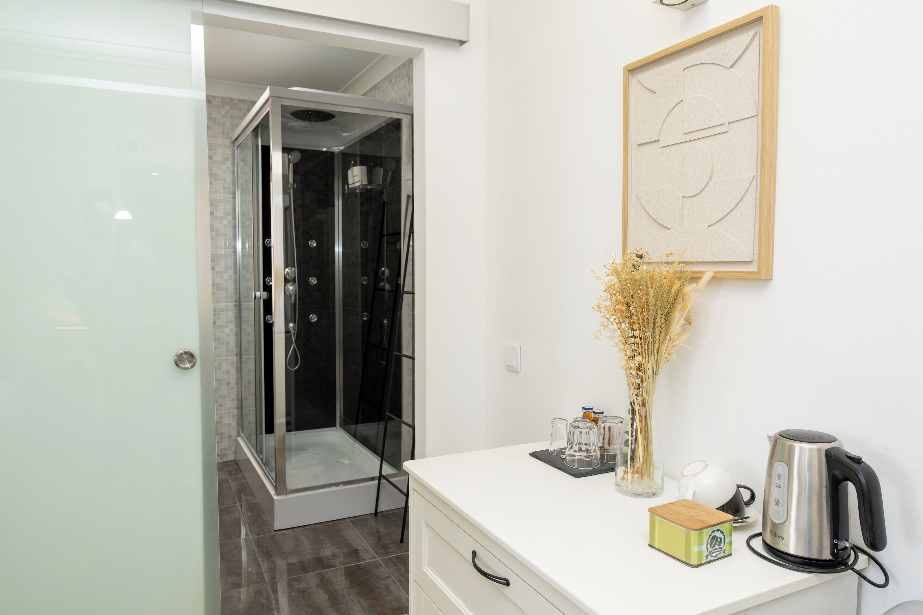 Een moderne badkamer met een douche, een wit aanrecht, een waterkoker en een lijst met abstracte kunst.