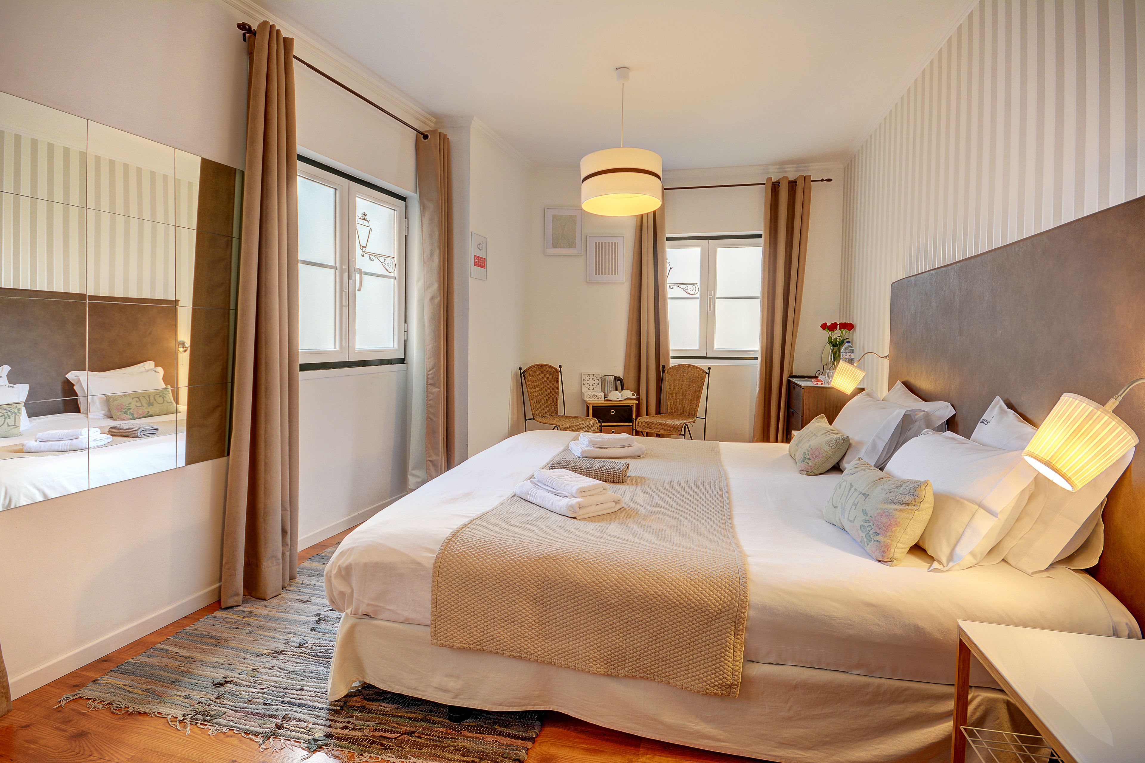 A well-lit hotel room with a large bed, a bedside table, a chair, and a mirror.