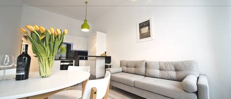 A modern kitchen with white cabinets, a dining table with chairs, and a grey sofa.
