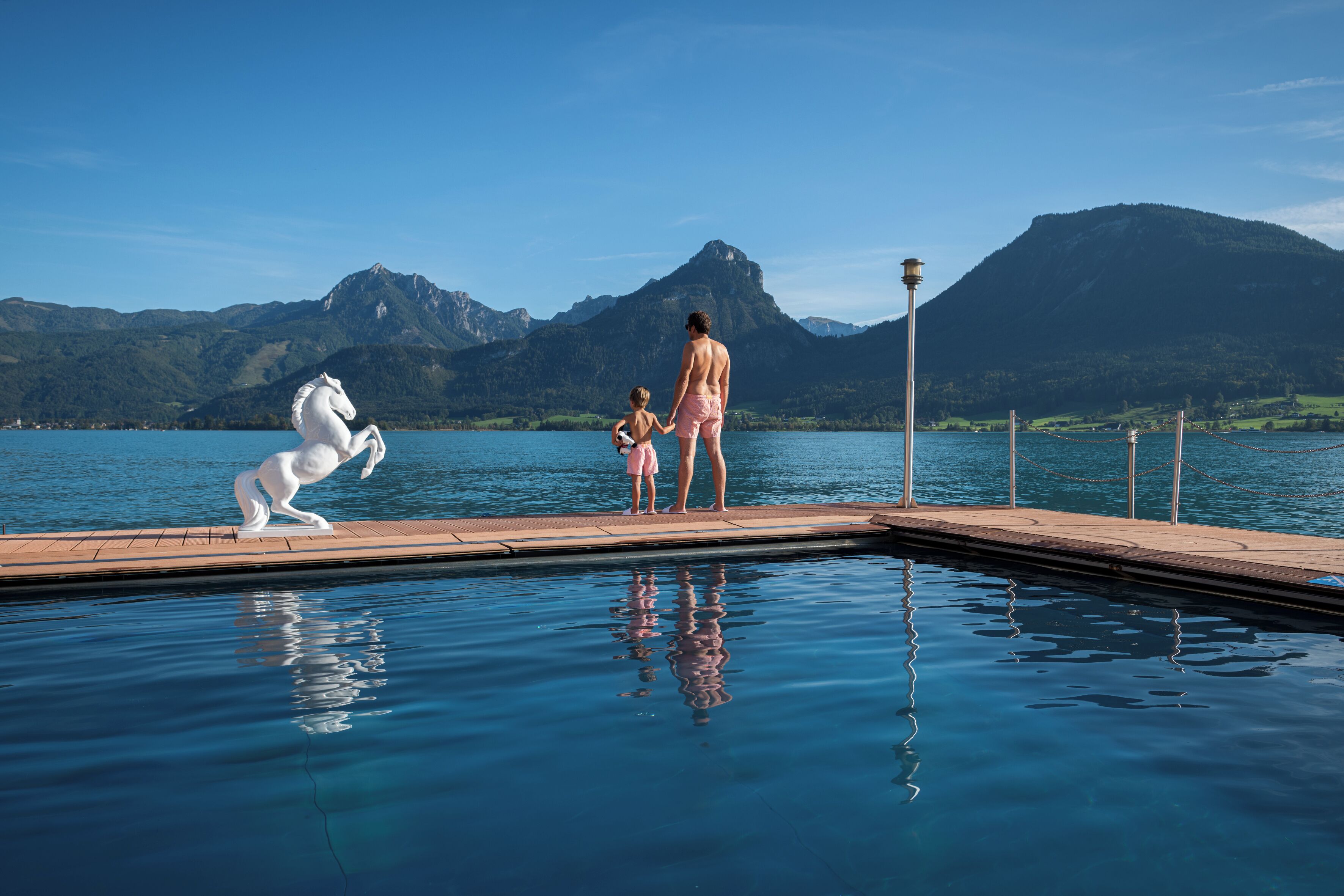 A swimming pool with a statue of a horse, a mountain in the background, and a person standing on the edge.