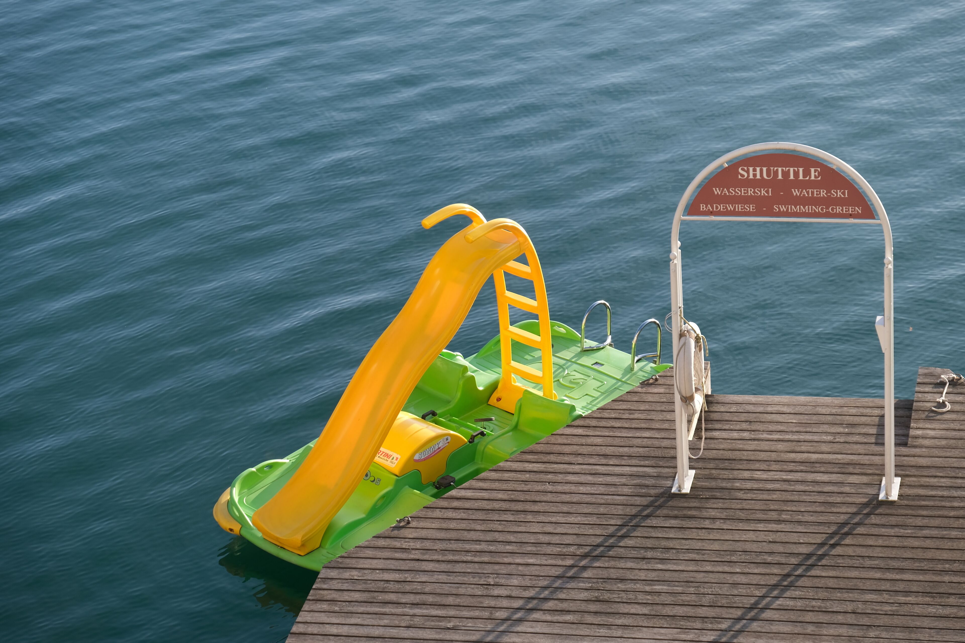 A wooden dock with a yellow and green slide and a shuttle sign indicating nearby locations.